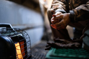 Hunter warming hands by a propane heater at a hunting camp before a propane cylinder refill
